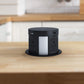 Black retractable pop up outlet with wireless charging top installed in a wood countertop